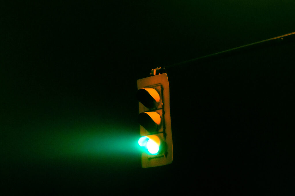 A green traffic light at night where the green light is glowing out into the darkness.