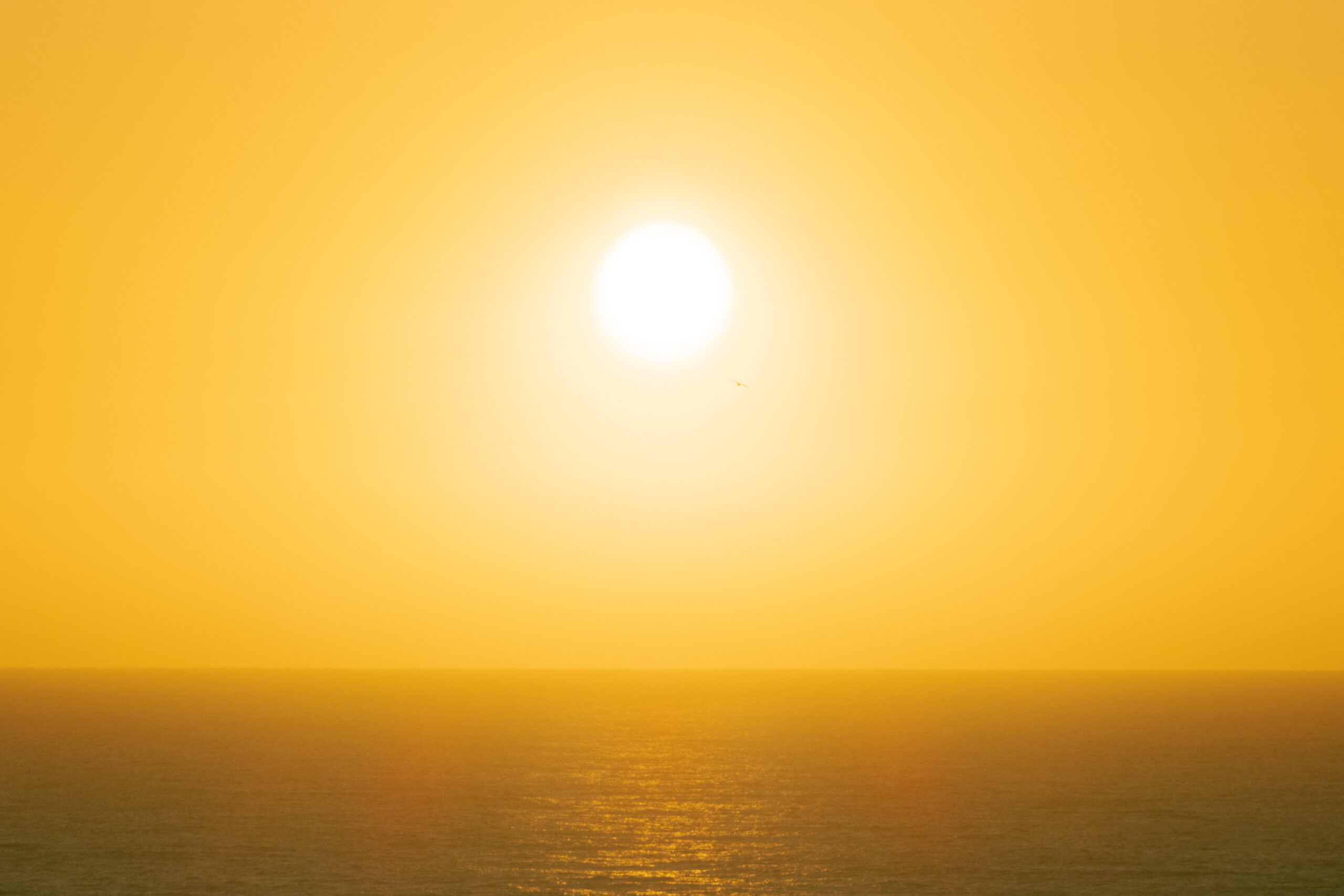 A bright yellow sky is lit by the sun in the centre of the image, the ocean visible below. 